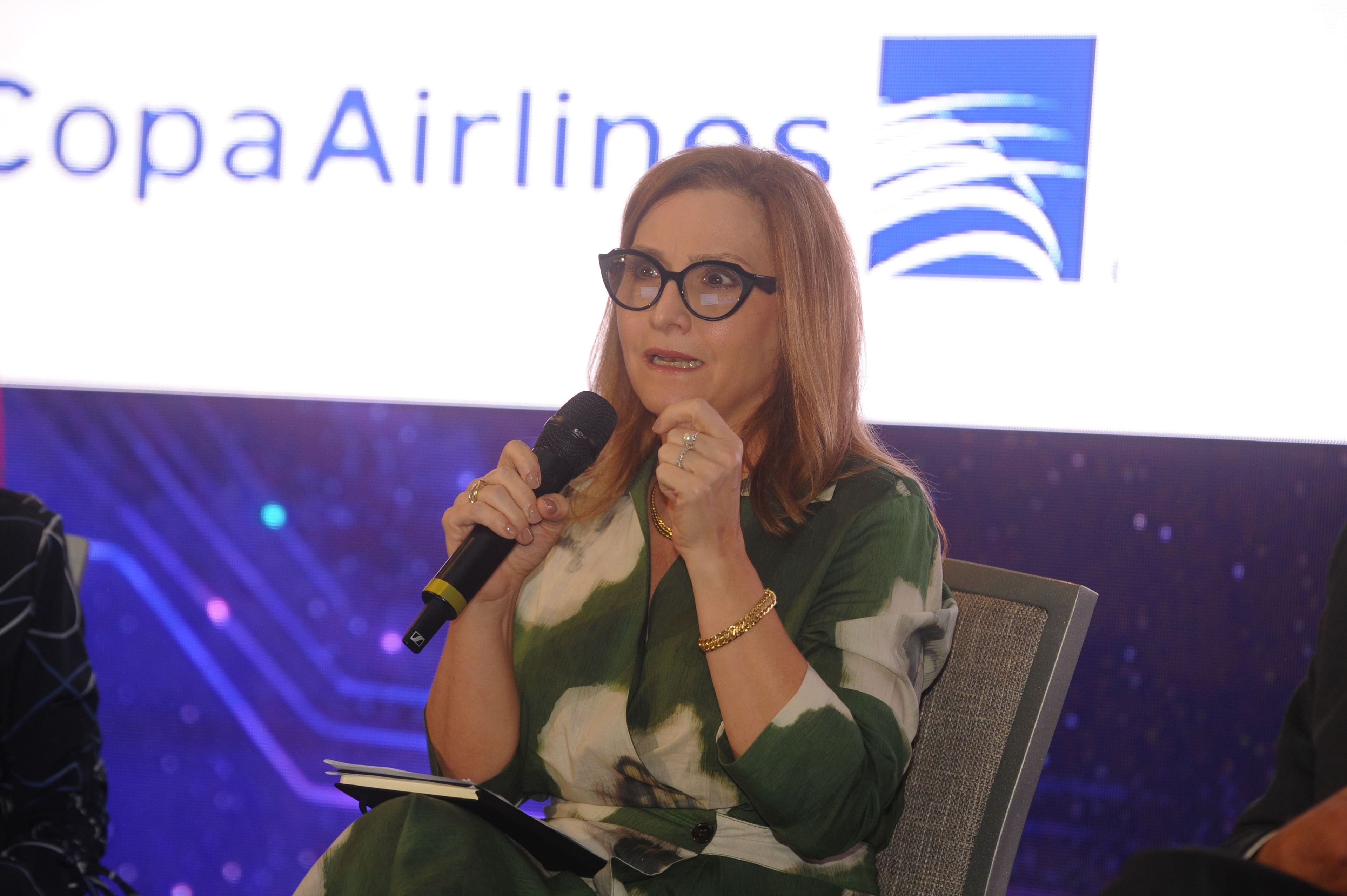 Lourdes M. Pérez con micrófono frente al logo de Copa Airlines en el Foro Empresarial WISS Latam 2026