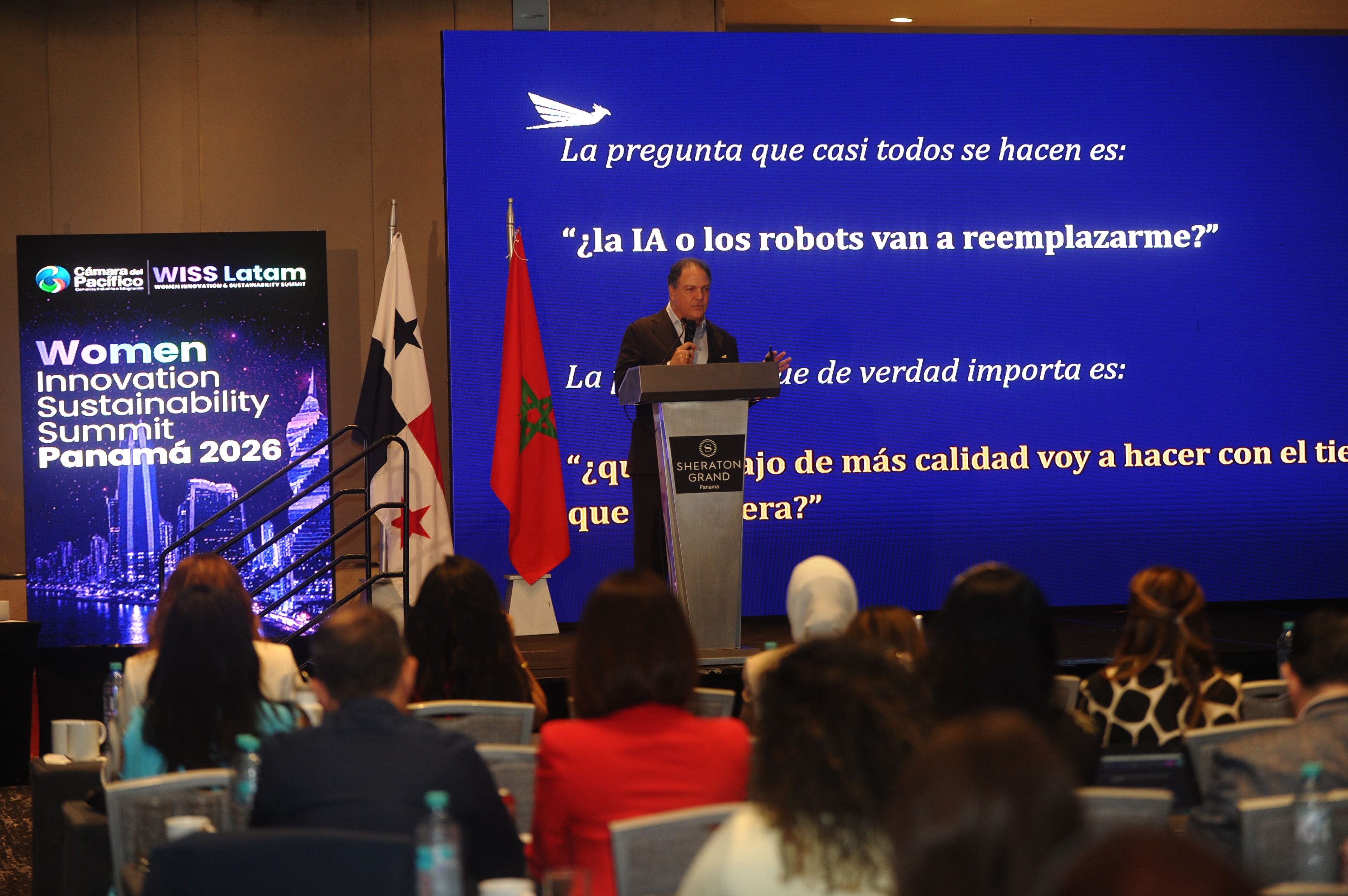 Ponente en el podio con pantalla "¿la IA o los robots van a reemplazarme?" — Foro Empresarial WISS Latam 2026