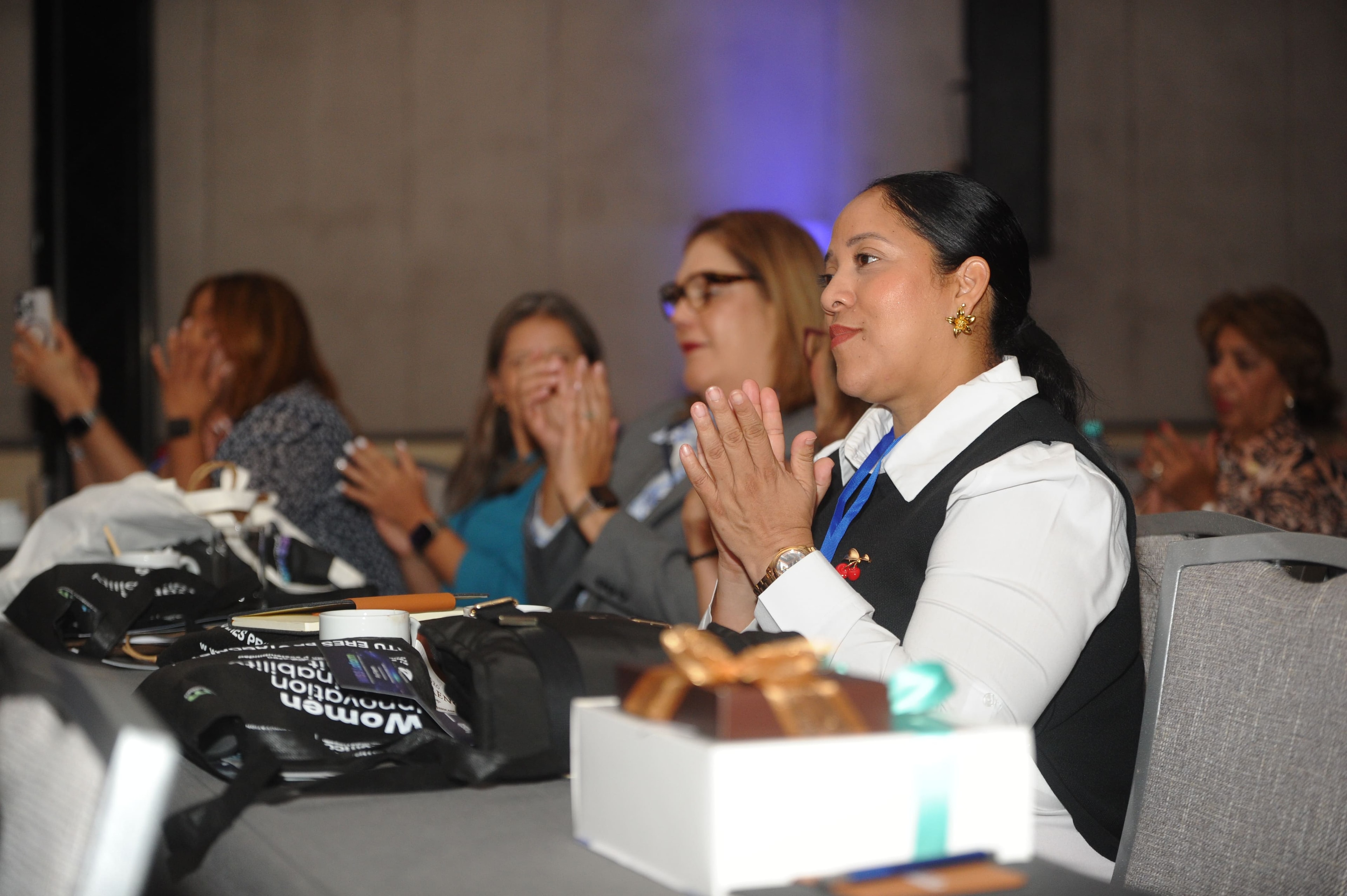 Asistente aplaudiendo en el salón del Foro Empresarial WISS Latam 2026 con bolsas WISS en la mesa