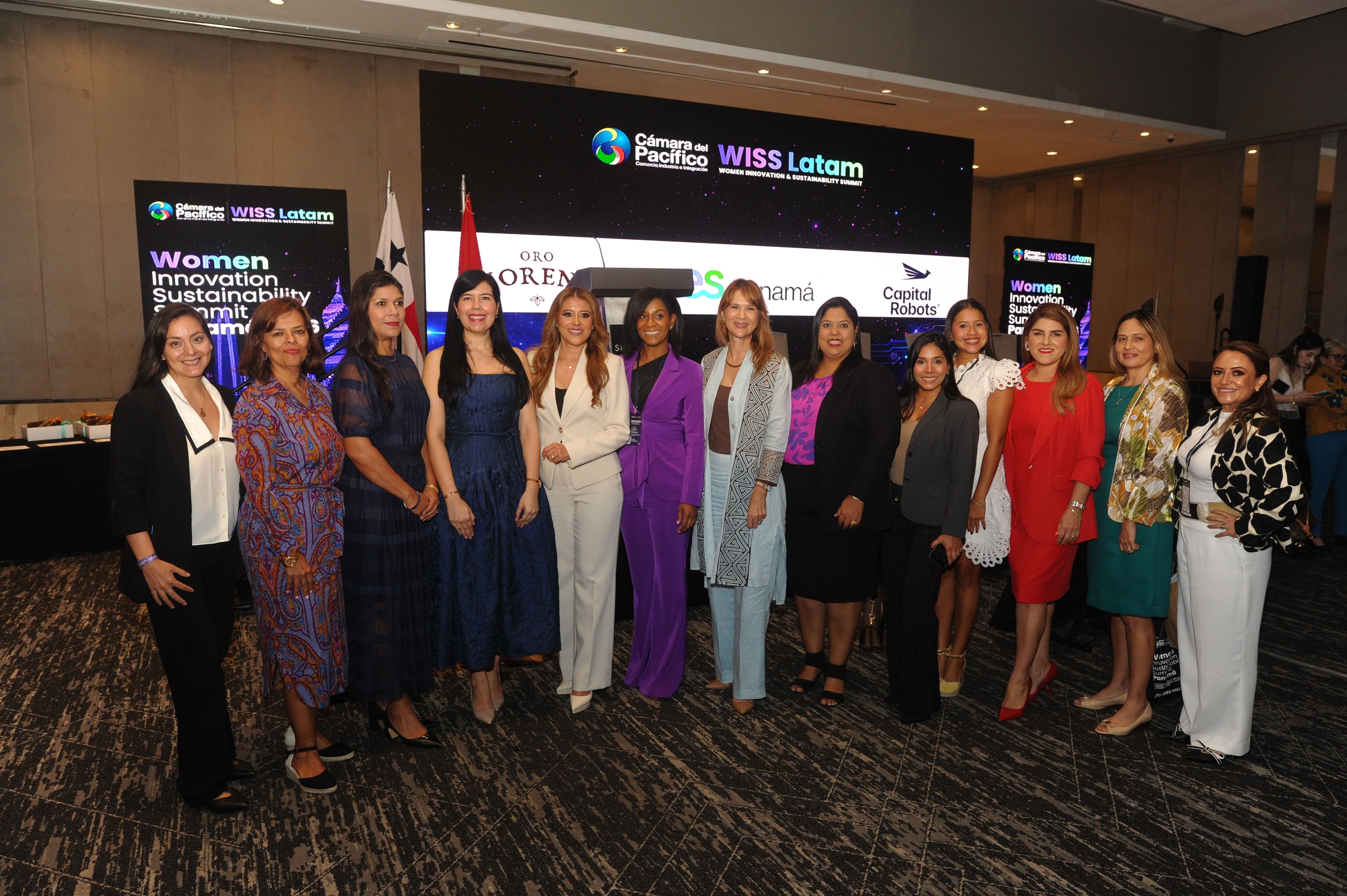 Grupo de más de doce mujeres posando frente a pantalla WISS Latam con logos Oro Moreno, SV y Capital Robots — Foro Empresarial 27 Ago 2026