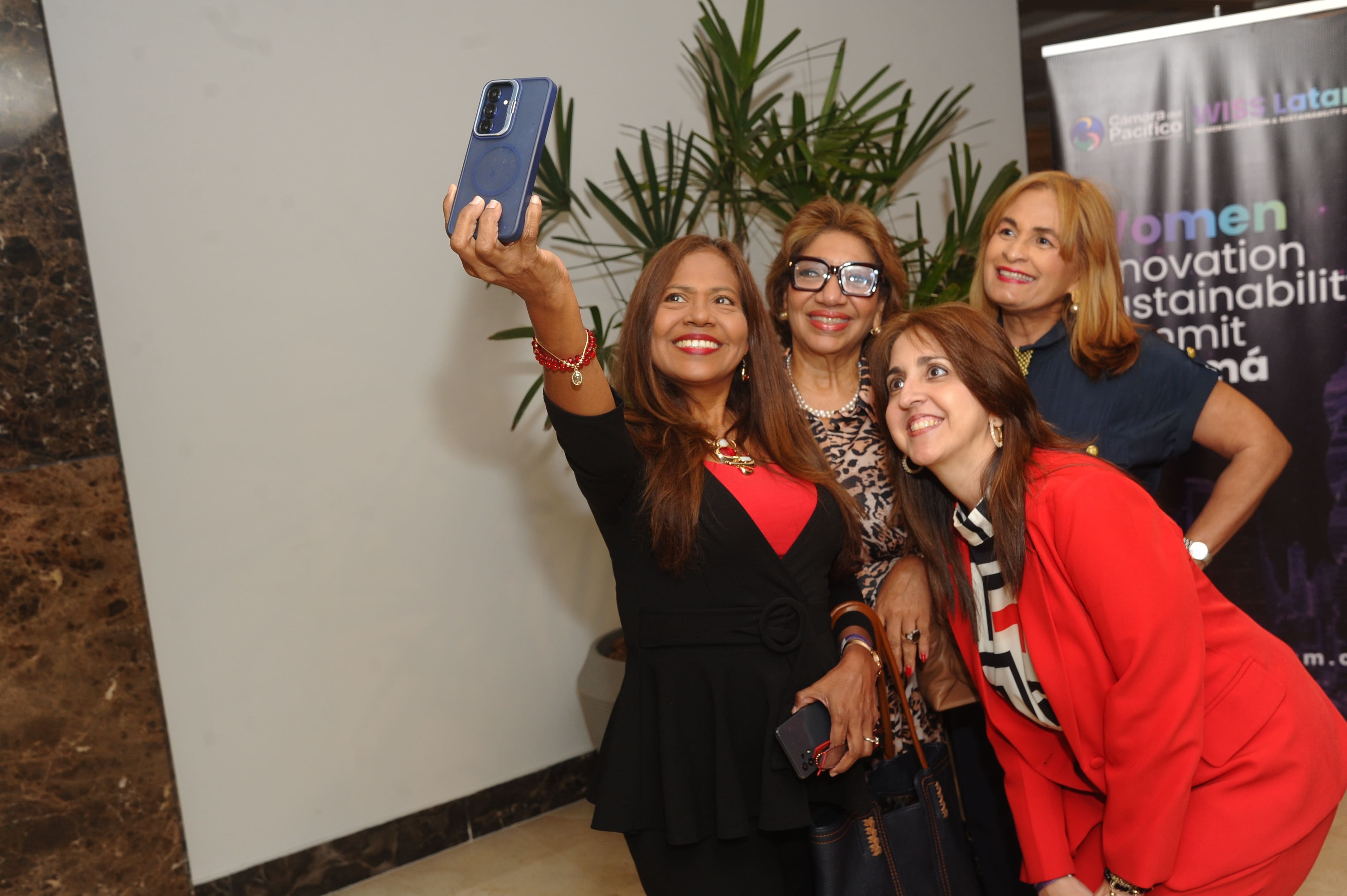 Cuatro mujeres tomándose selfie en el lobby frente a banner de WISS Latam y Cámara del Pacífico — Foro 27 Ago 2026